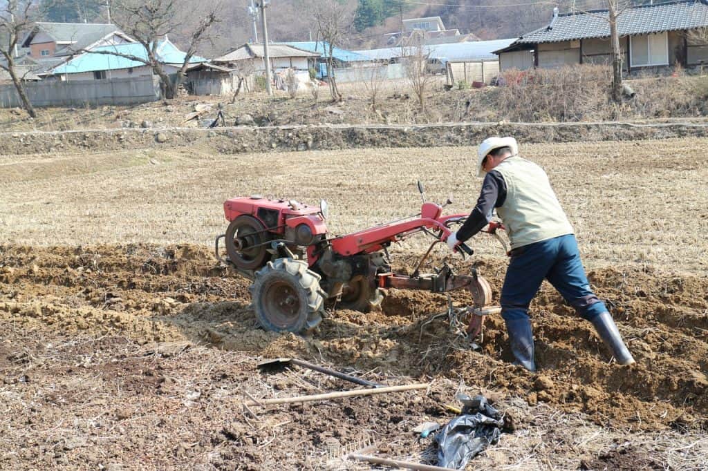 Man pushing a red tiller through the soil