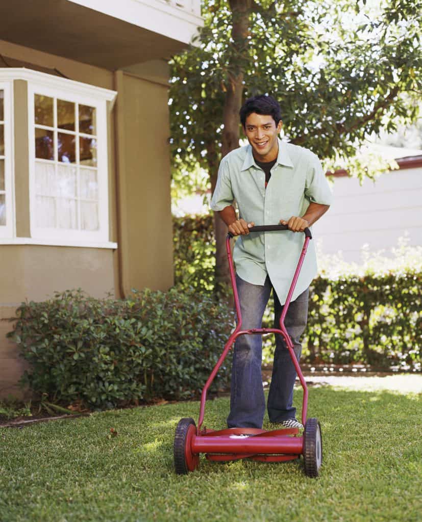 Man pushing a lawn mower in his yard to cut grass