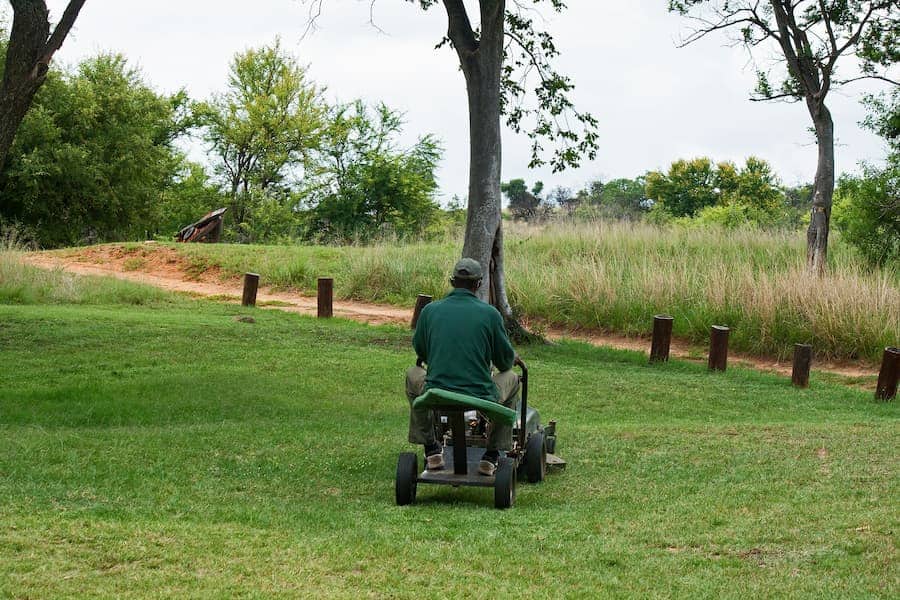 A guy in a green shirt rides a small lawnmower.