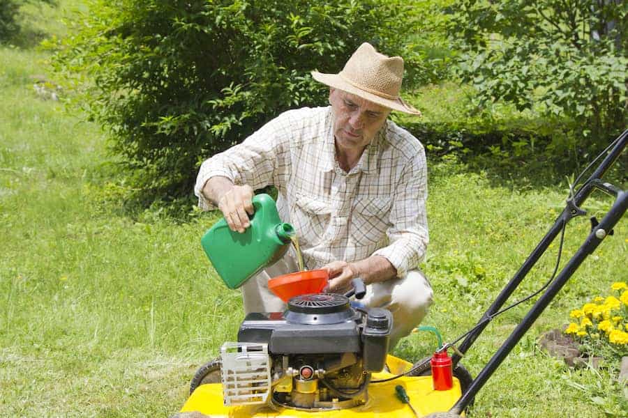 Mid age man adding oil to lawnmover