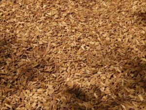 A pile of uneven sizes of brown woodchips on a sunny day