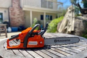 An orange Husqvarna chainsaw with a silver blade on top of a brown wooden table