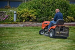A person wearing blue long sleeves shirt and denim pants is using a black and orange lawn mower to mow the lawn