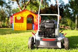 A black and gray lawn mower near a yellow and red playhouse on top of a green grass
