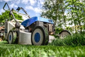 A blue and silver lawn mower mows the green grass overlooking the blue sky